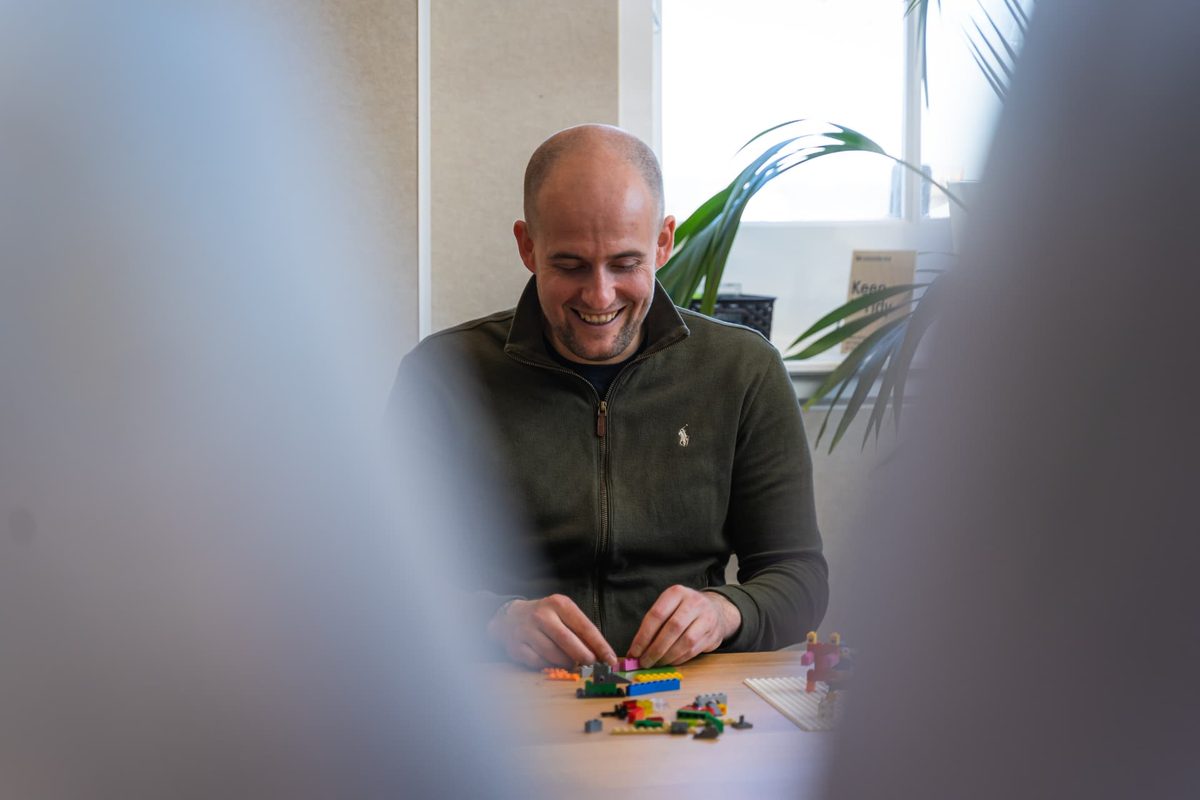 Lee Fitzpatrick smiling as he builds with Lego bricks at a bright office desk