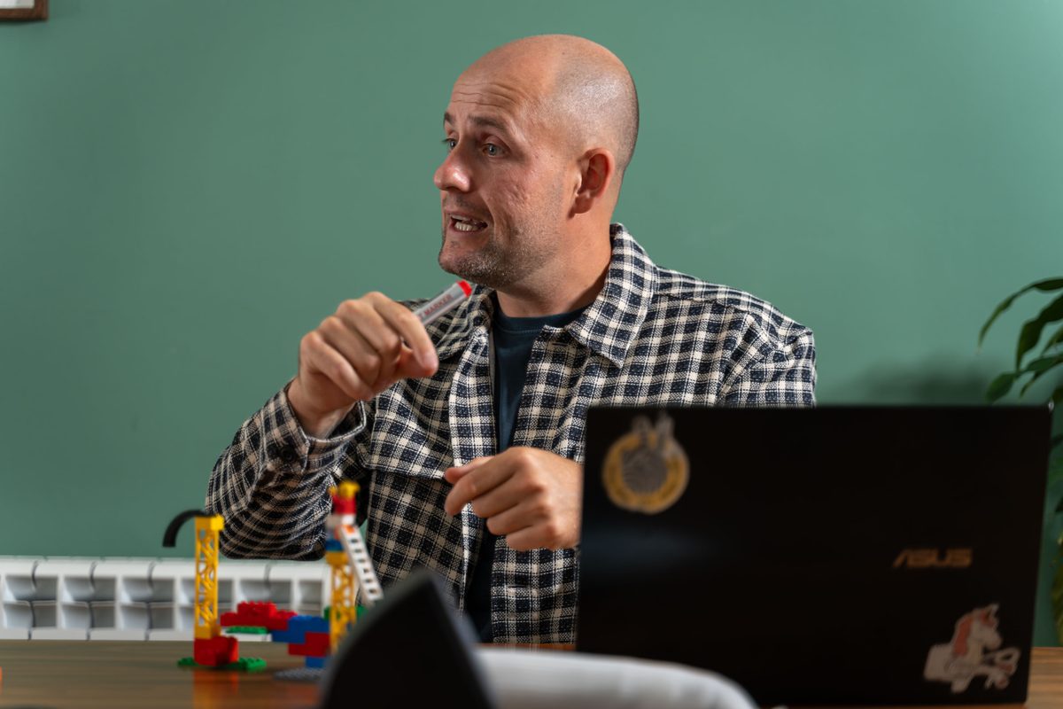Lee Fitzpatrick mid-sentence with a marker in hand, laptop and Lego models on the table